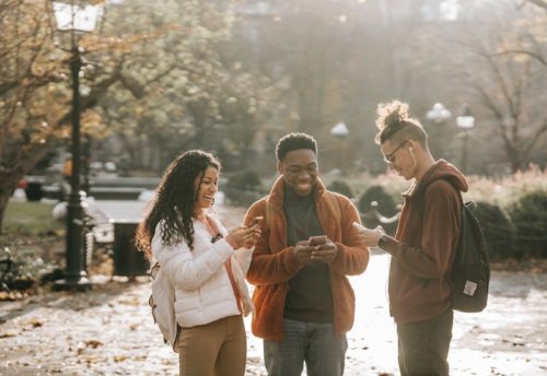 three young adults standing outside smiling and looking at phones